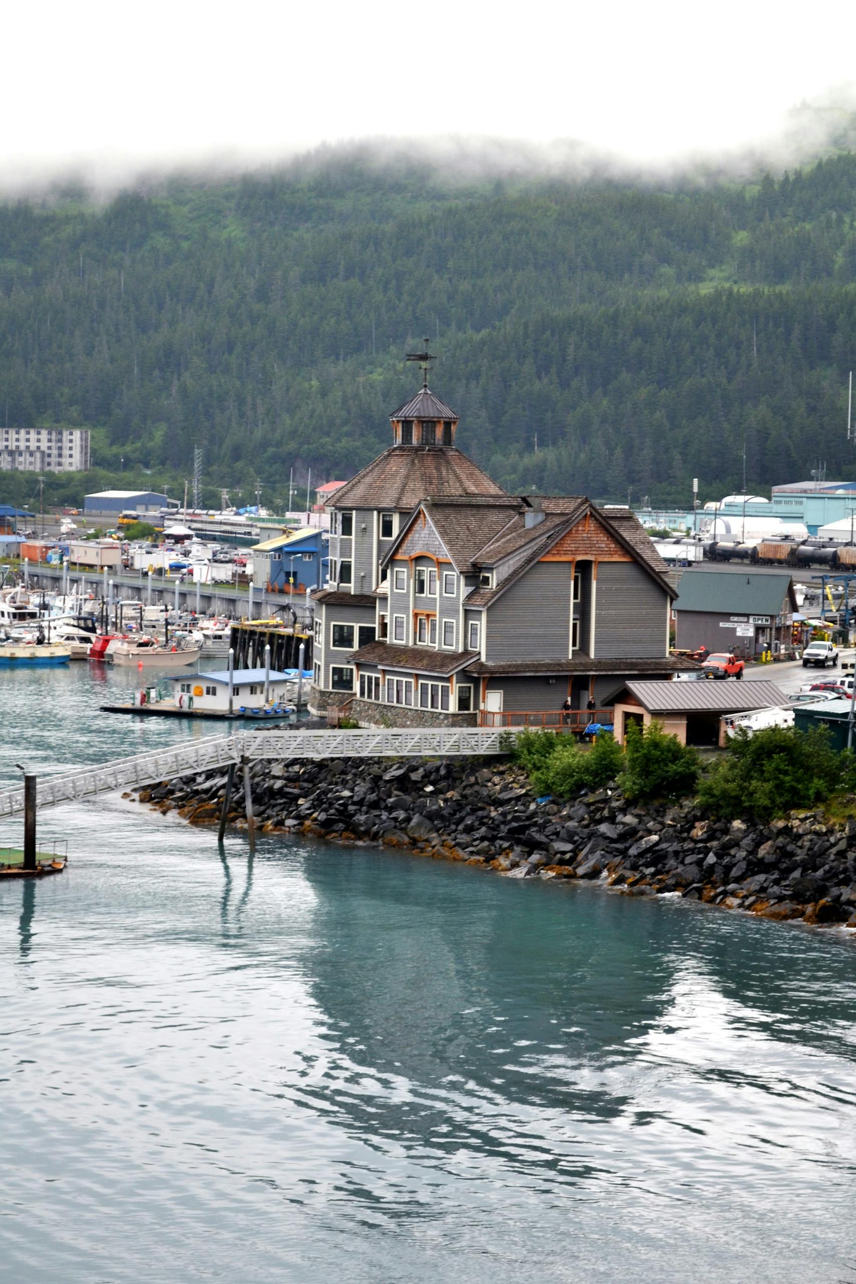 A beautiful view of the waterfront and marina in Whittier, Alaska, with lush green mountains in the background.