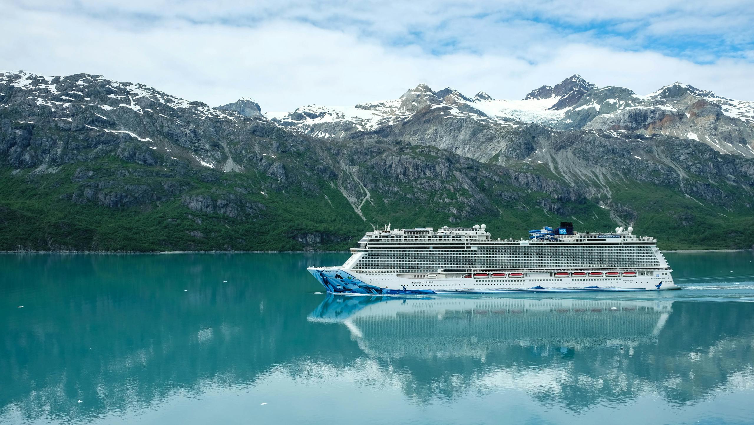 A majestic cruise ship sailing through clear waters with snowy mountains as a backdrop.