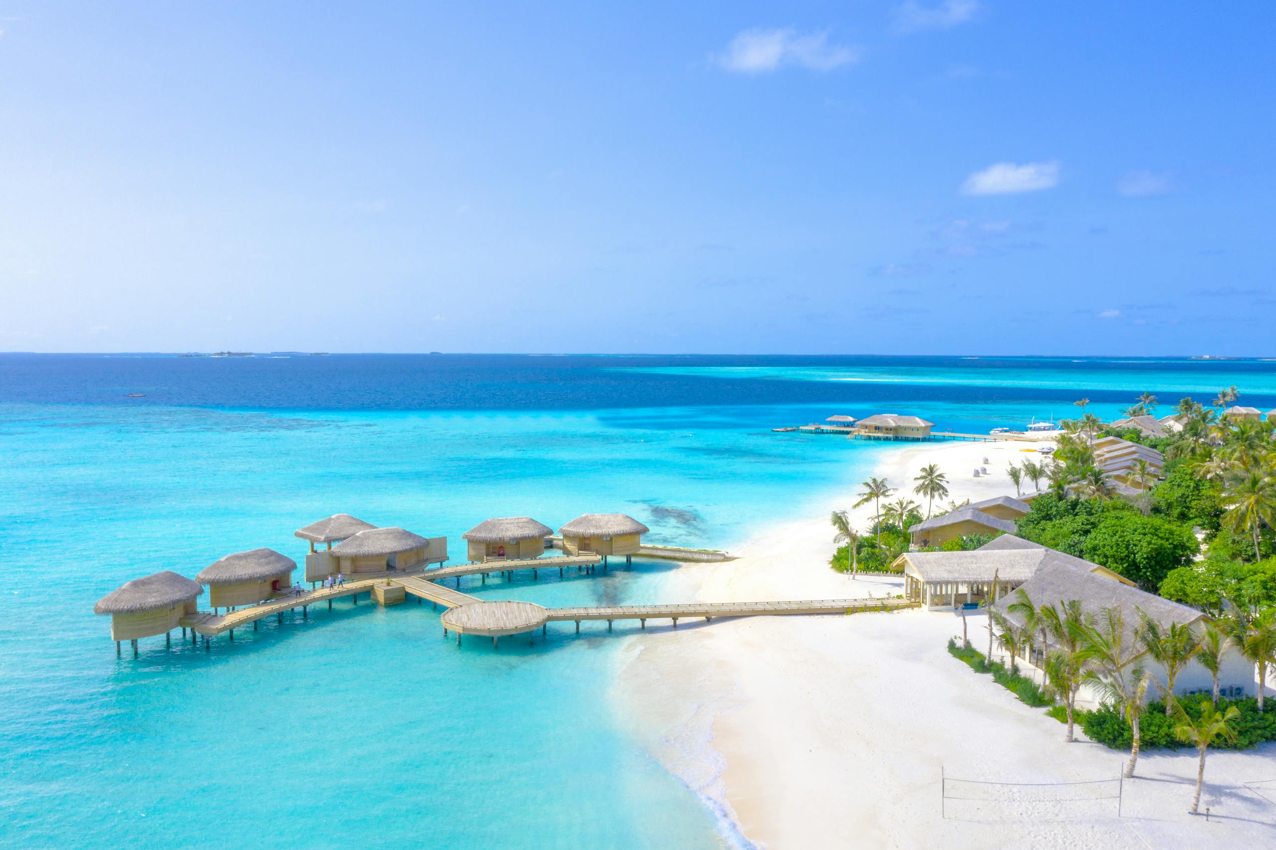 A pristine beach resort with overwater bungalows in the Maldives under a clear blue sky.
