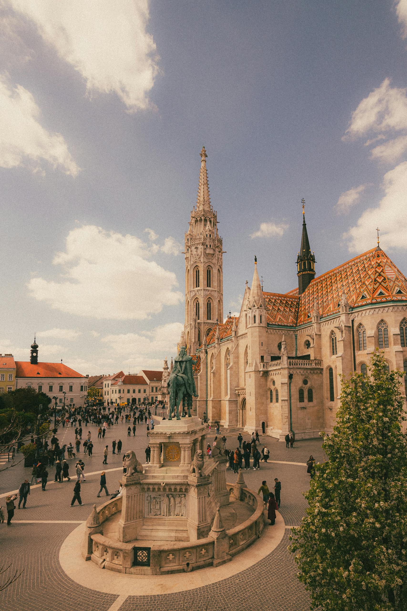 A scenic view of Matthias Church and the Holy Trinity Statue in a bustling square in Budapest, Hungary.