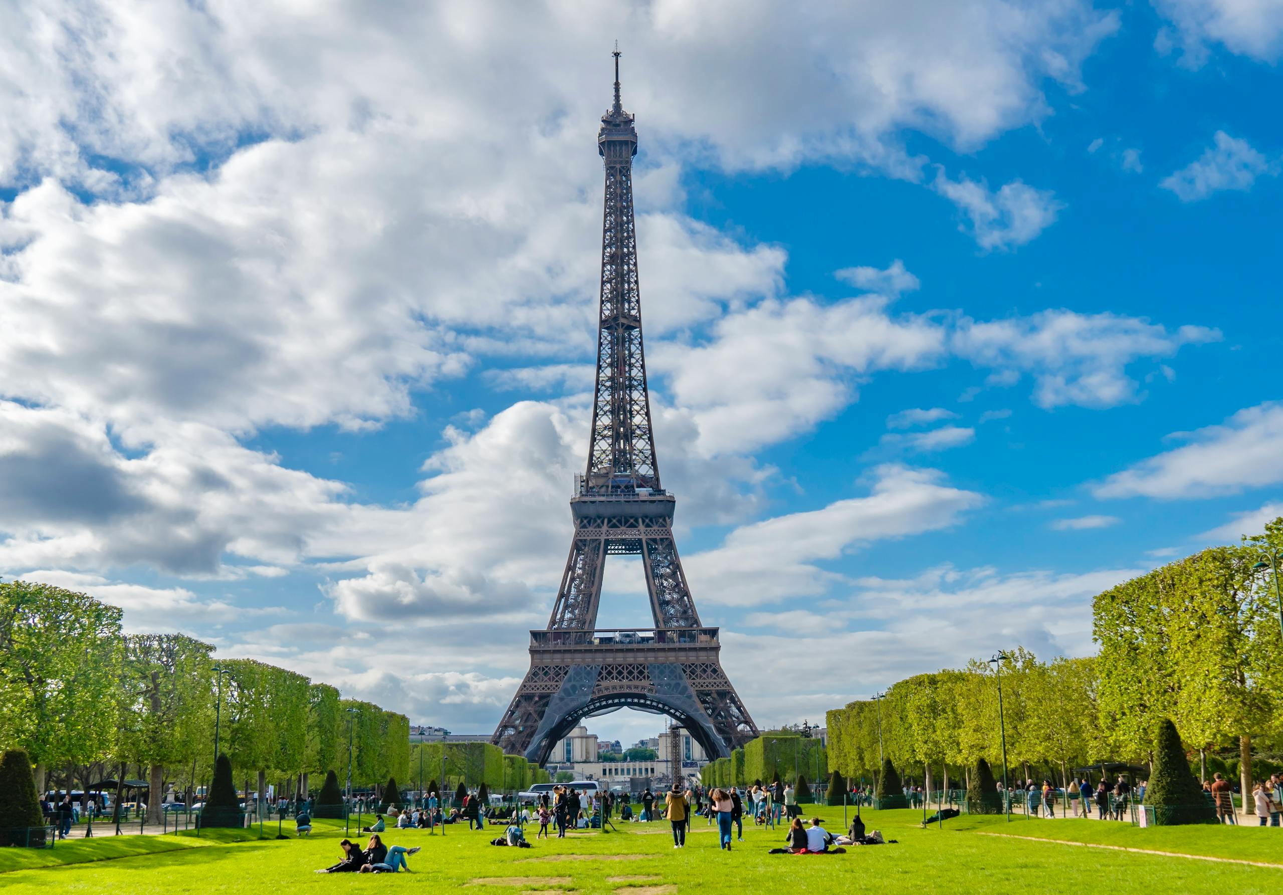 A scenic view of the Eiffel Tower with people enjoying the sunny day in Paris, France.