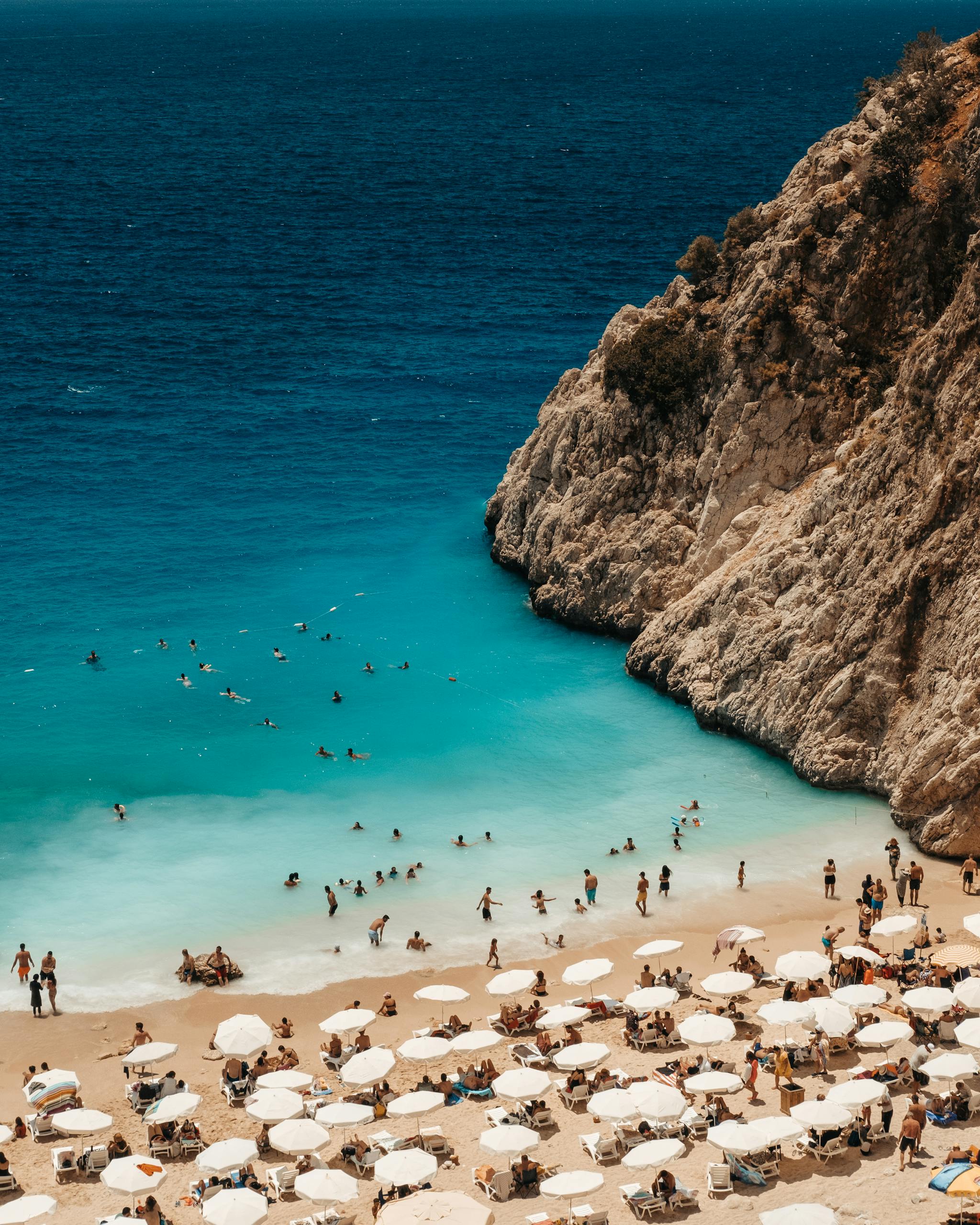 A stunning aerial view of a crowded beach in Antalya, Turkey with turquoise waters and beach umbrellas.