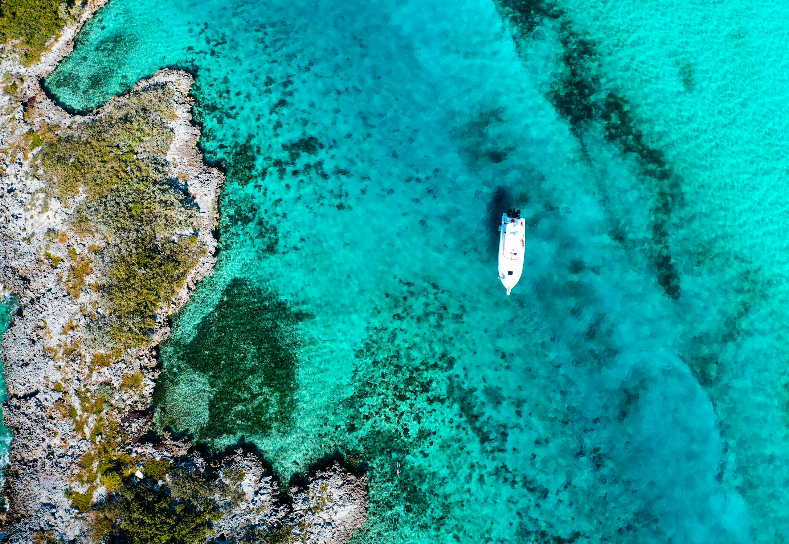 Aerial shot of a boat floating in the turquoise waters of the Bahamas, showcasing vibrant coral reefs.