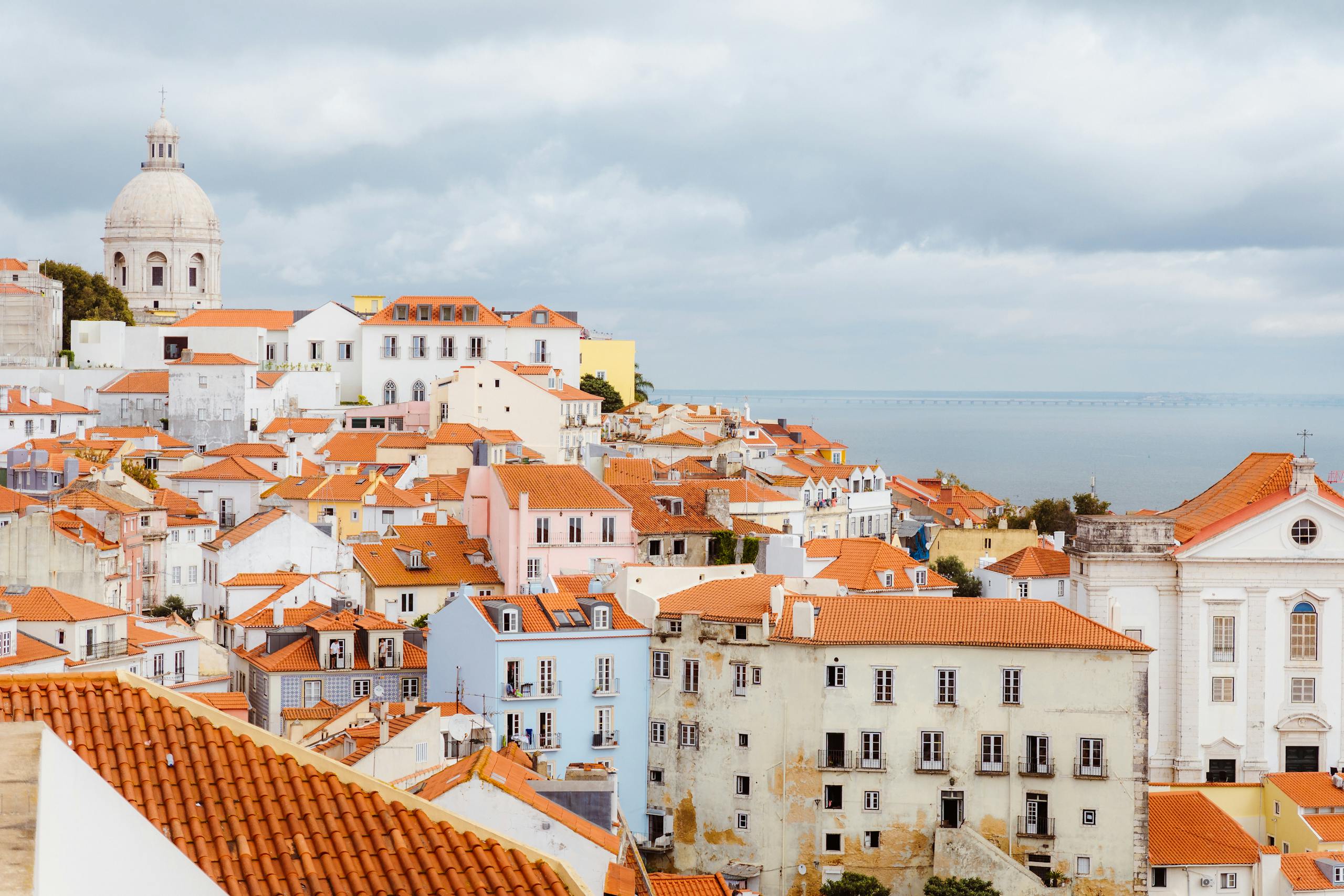 Beautiful panoramic view of Lisbon's Alfama district with red rooftops and the sea in the background.