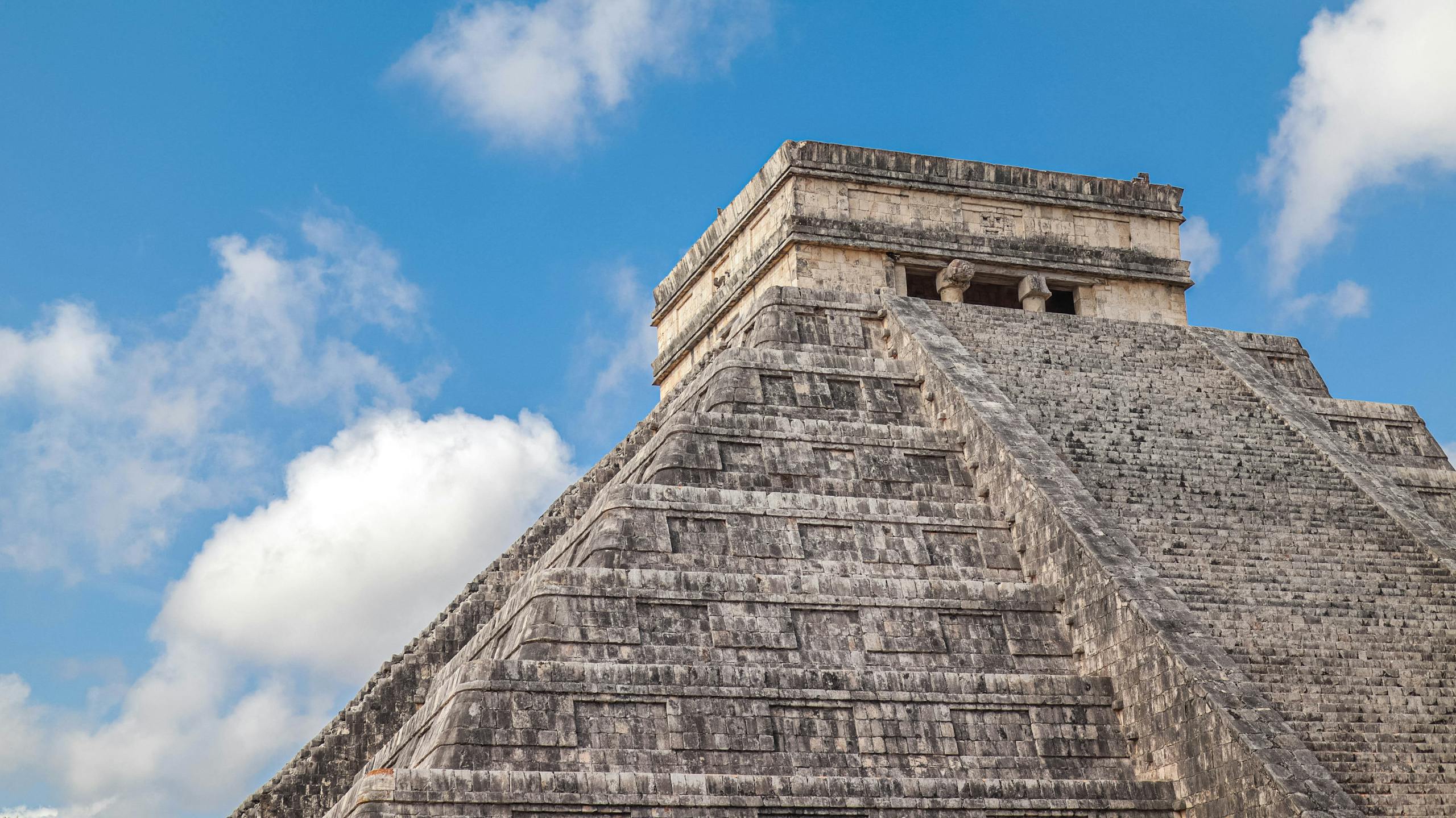Close-up view of the Pyramid of Kukulcan at Chichen Itza under a clear blue sky with scattered clouds.