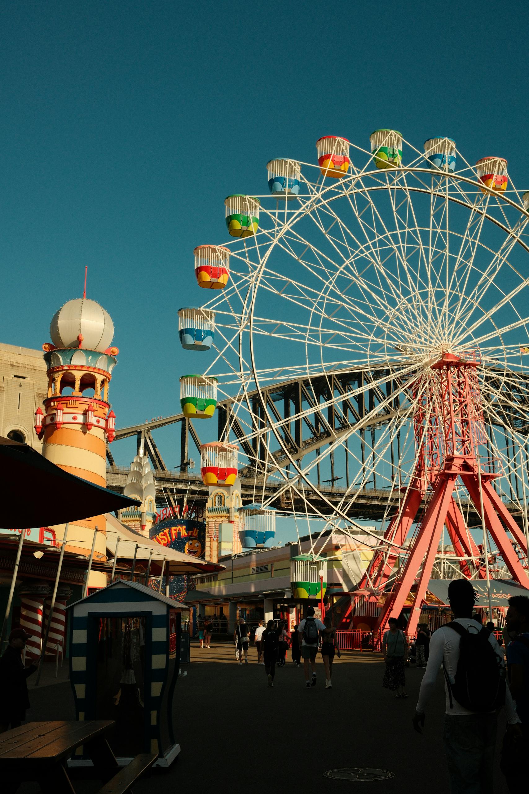 Colorful Ferris wheel at Sydney's Luna Park with Sydney Harbour Bridge in background, vibrant and lively.
