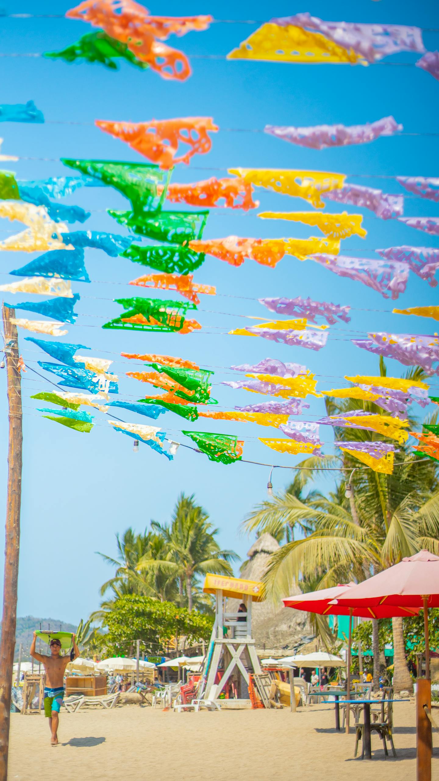 Colorful flags flutter above a lively beach scene in Sayulita, Mexico, capturing the essence of summer.