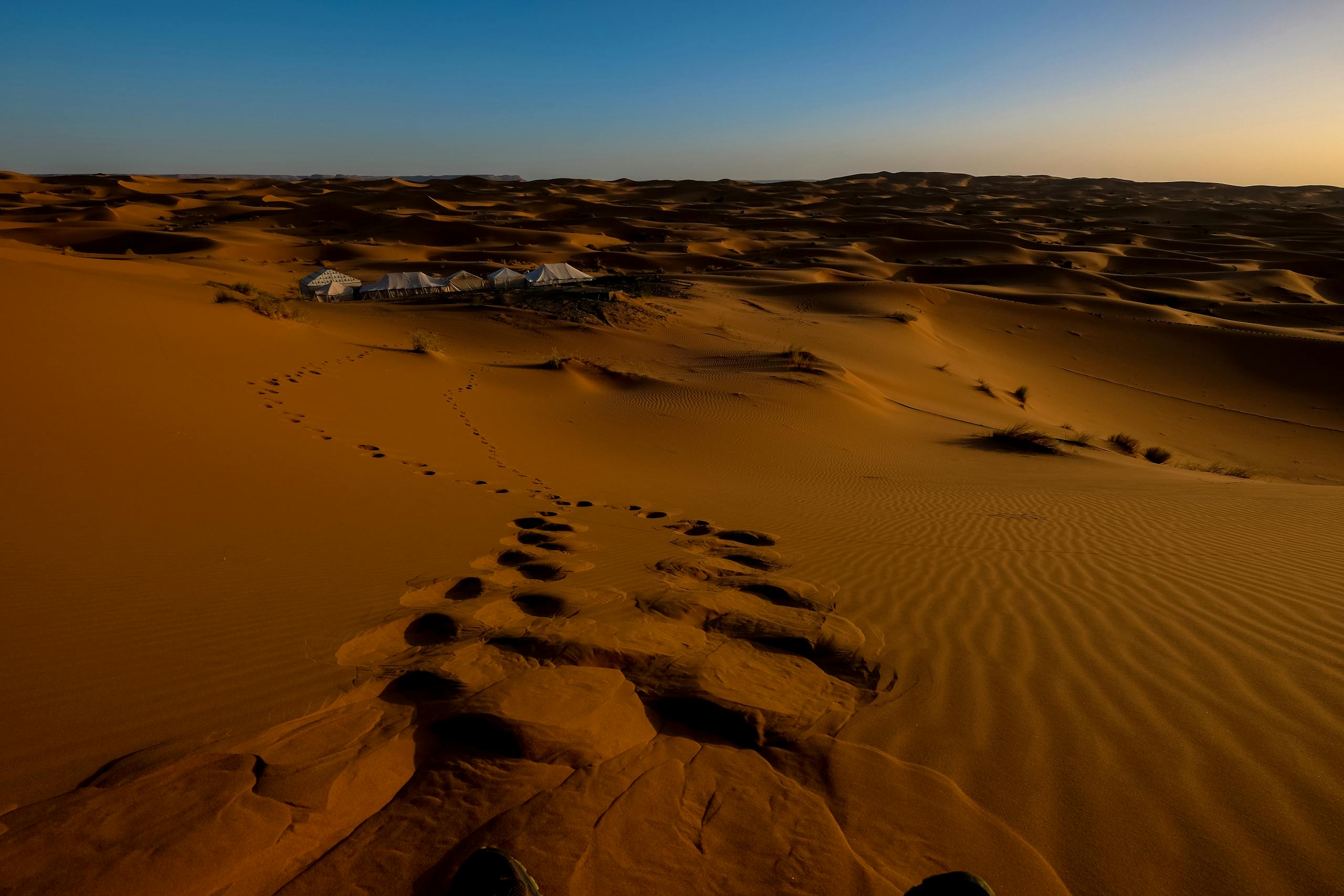 Golden sand dunes and distant tents at sunset in the Moroccan Sahara, Ksar Tanamouste.
