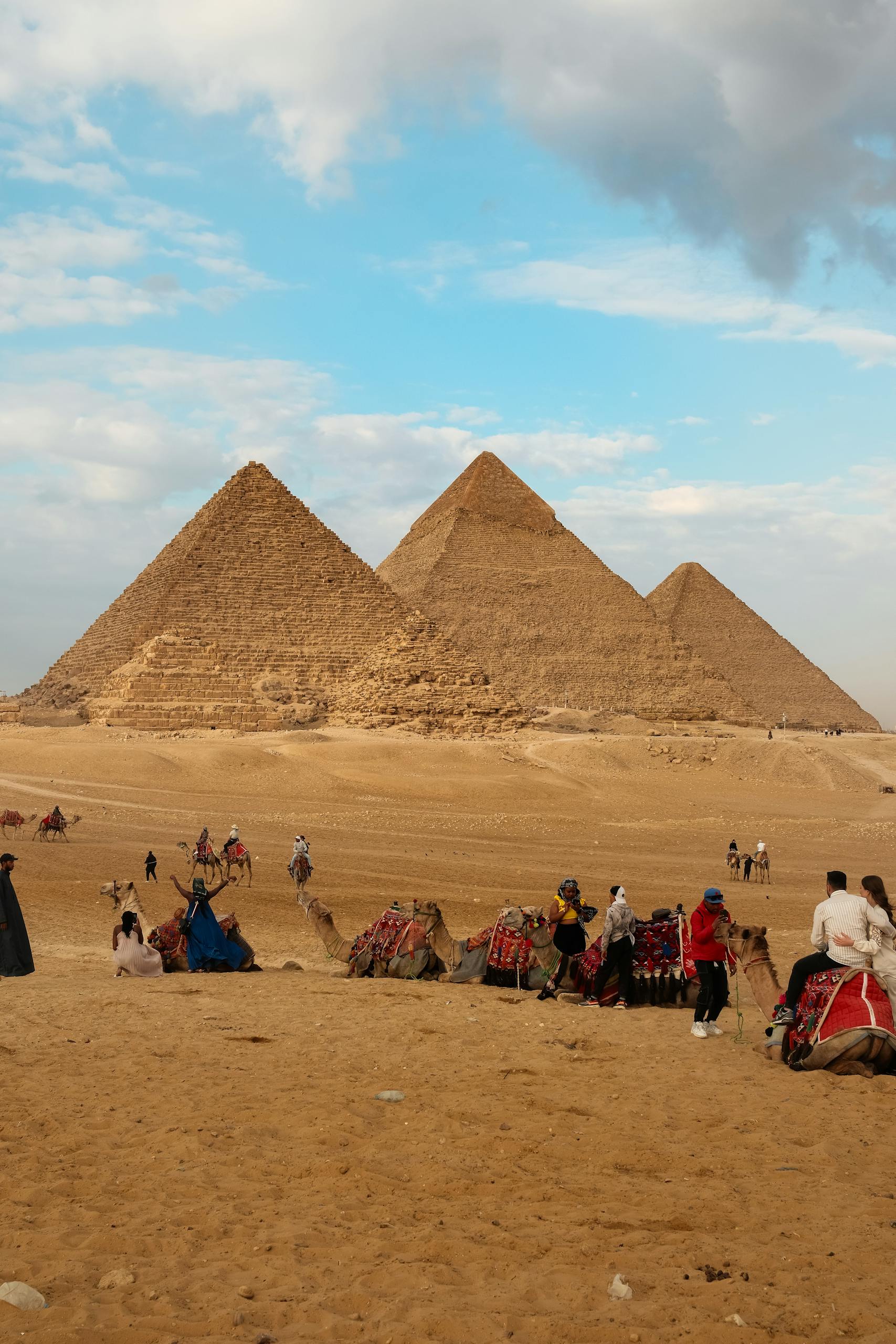 Iconic view of the Great Pyramid of Giza with tourists and camels under a bright sky.