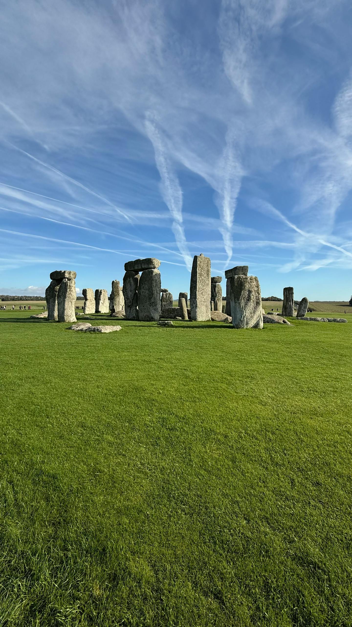 Stonehenge on a sunny day with vibrant green grass and blue sky, England.
