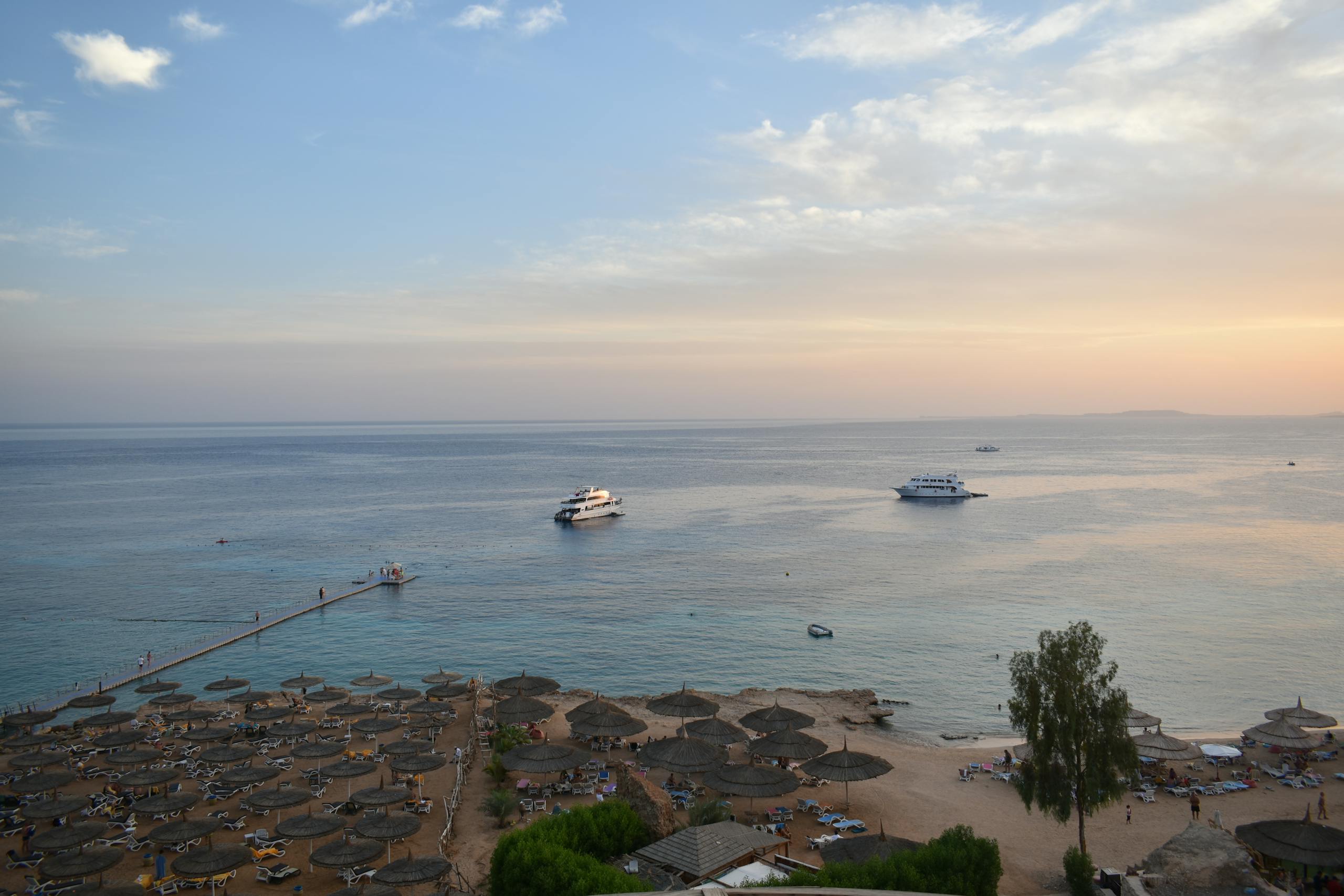 Stunning aerial view of Sharm El Sheikh's beach and sea during sunset with boats and parasols.