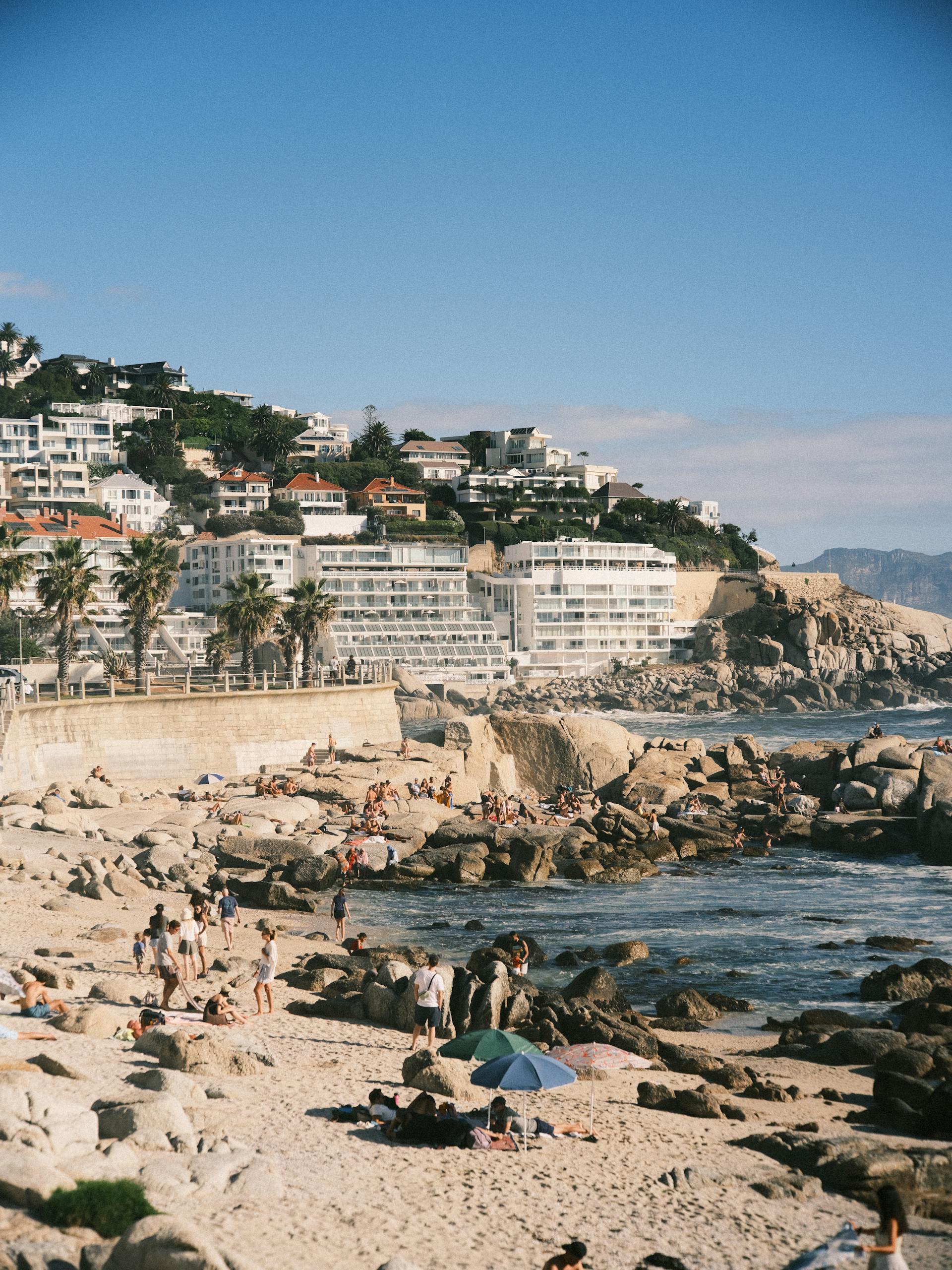 Sunlit beach with people enjoying summer by the sea in Cape Town, South Africa.