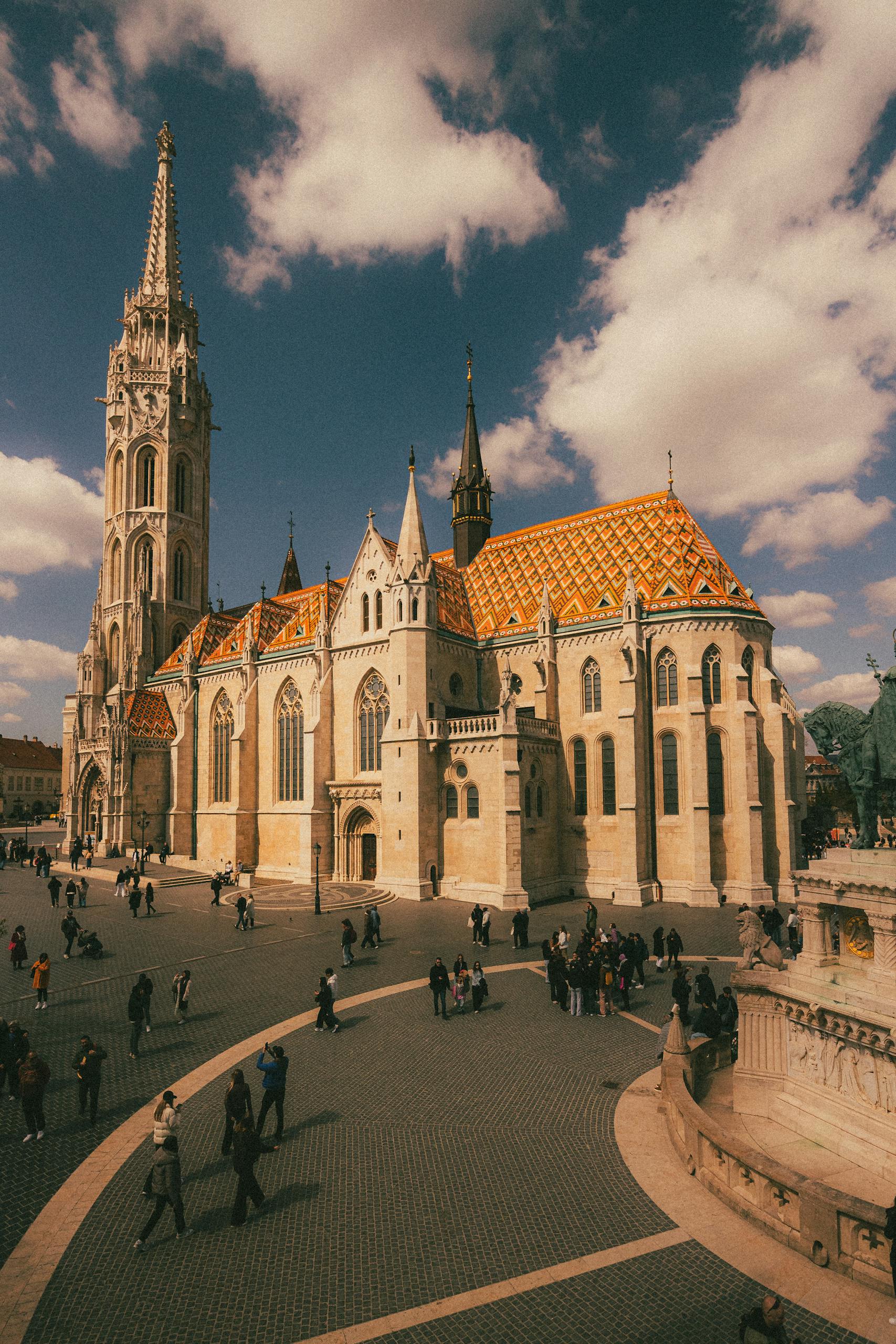 The iconic Matthias Church with vibrant roof tiles in Budapest, bustling with tourists on a sunny day.