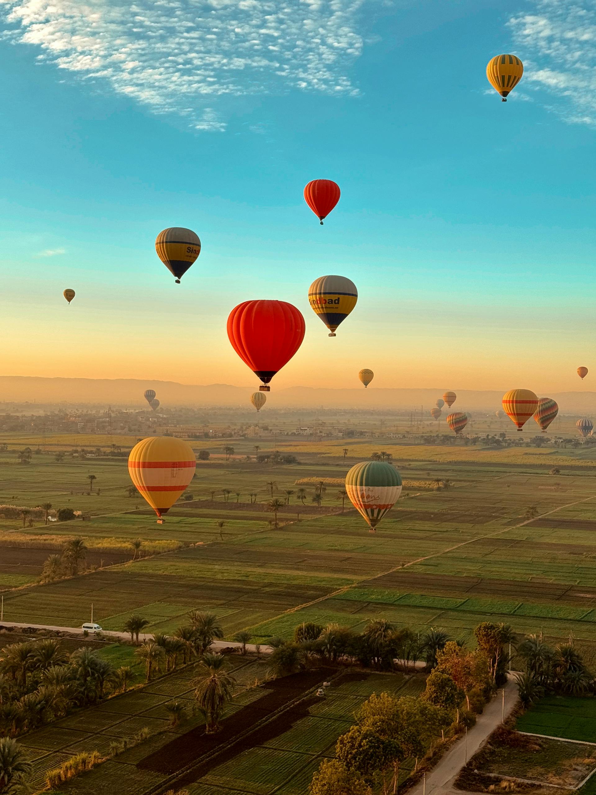 Vibrant hot air balloons soar over green fields in Luxor, Egypt at sunrise.
