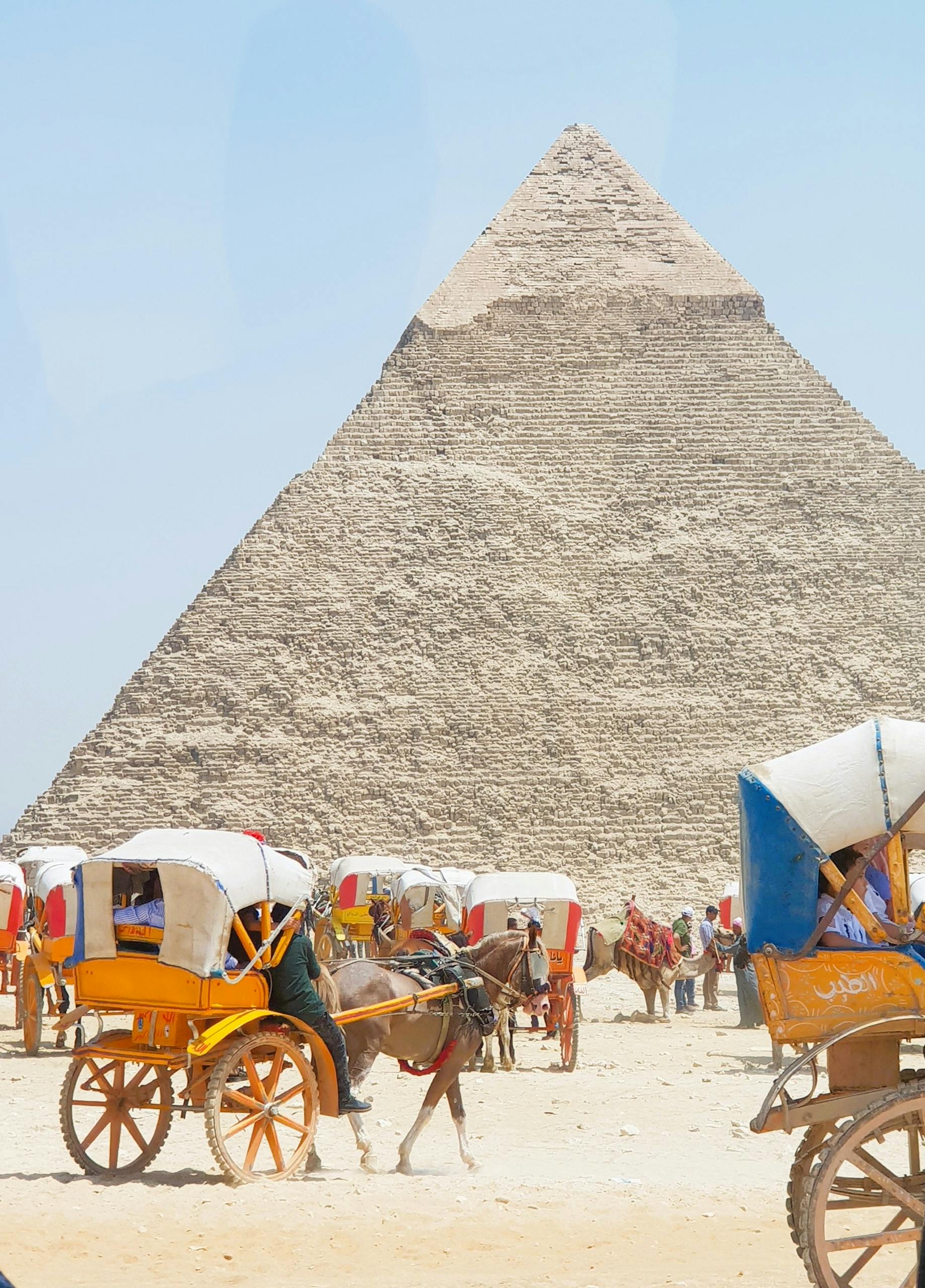 Vibrant scene of horse-drawn carriages near the iconic Great Pyramid of Giza in Egypt.