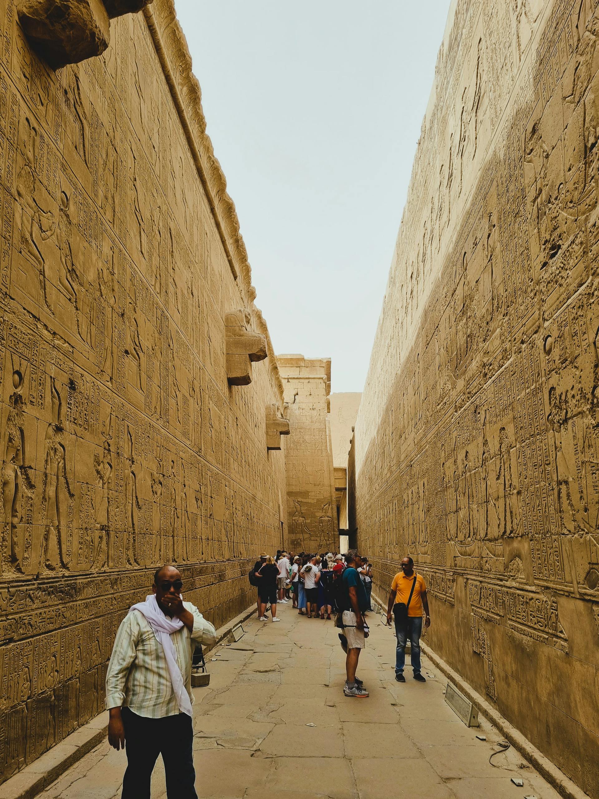 Visitors walk through a corridor of an ancient Egyptian temple with hieroglyphic carvings.