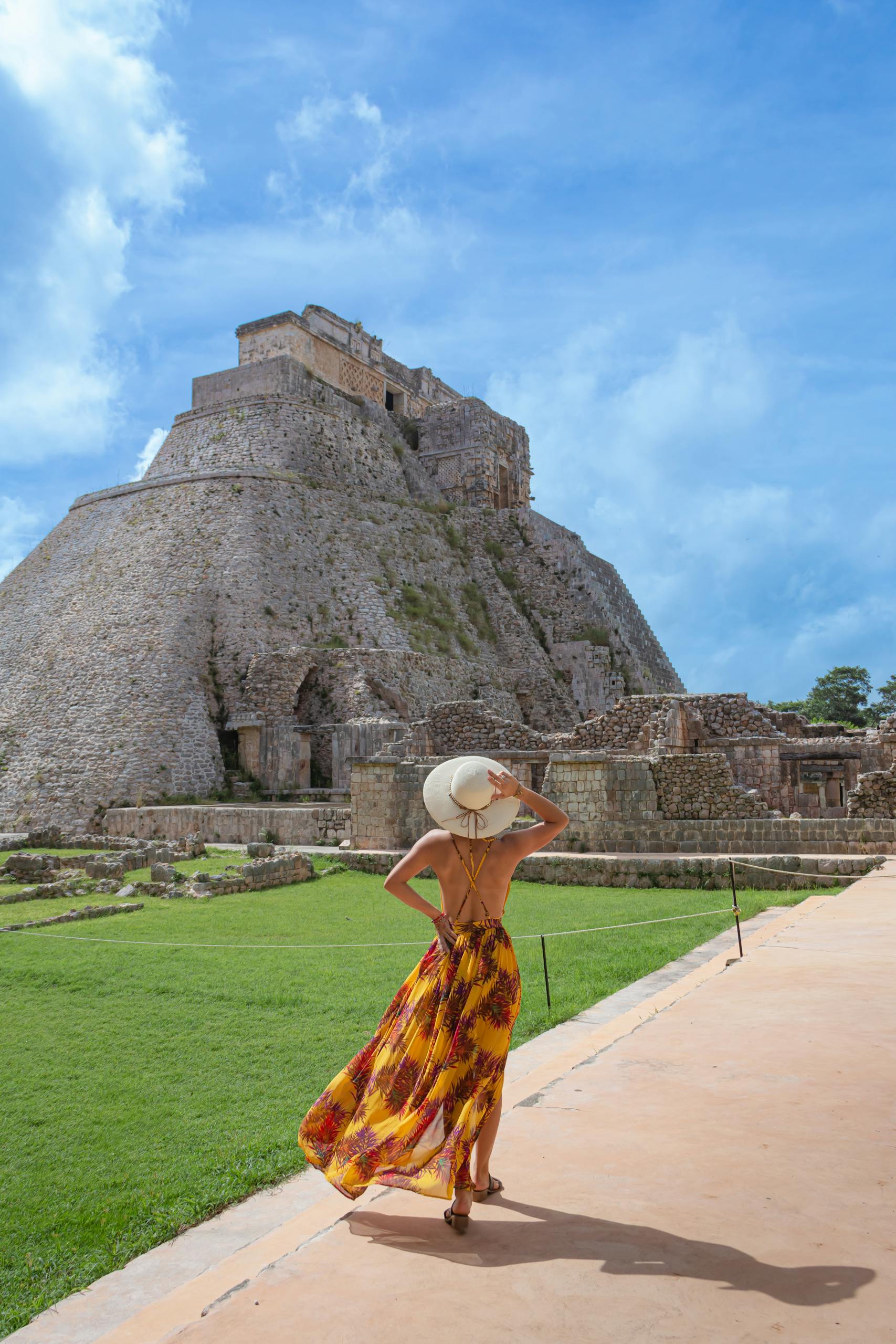 Woman in summer dress exploring the pyramid of the magician in Uxmal, Mexico, on a sunny day.