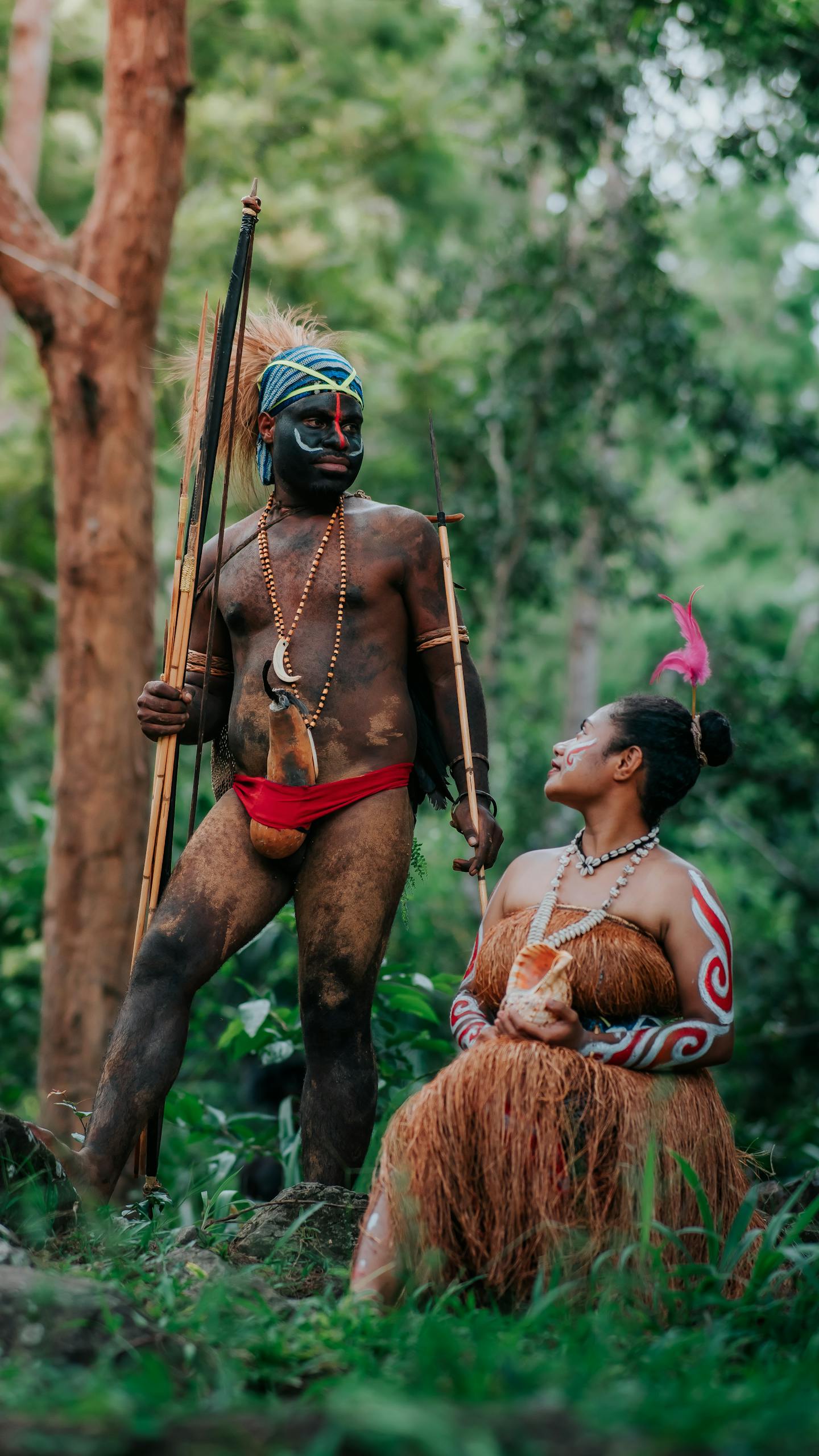 A man and woman in traditional Papua clothing in a lush forest setting.