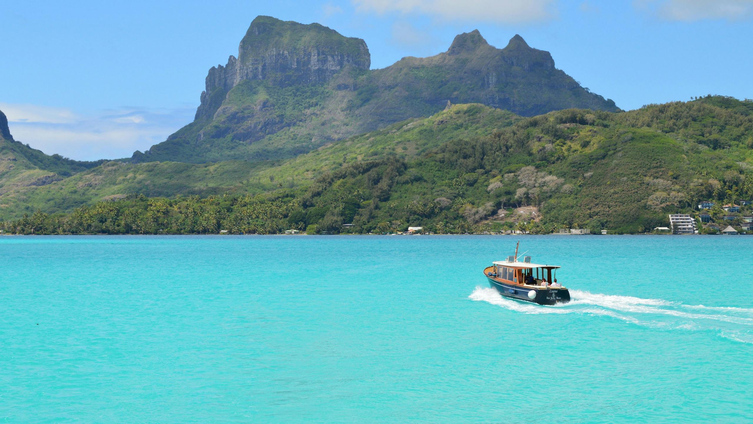 A scenic view of a boat cruising on the turquoise waters near lush mountains in Bora Bora.