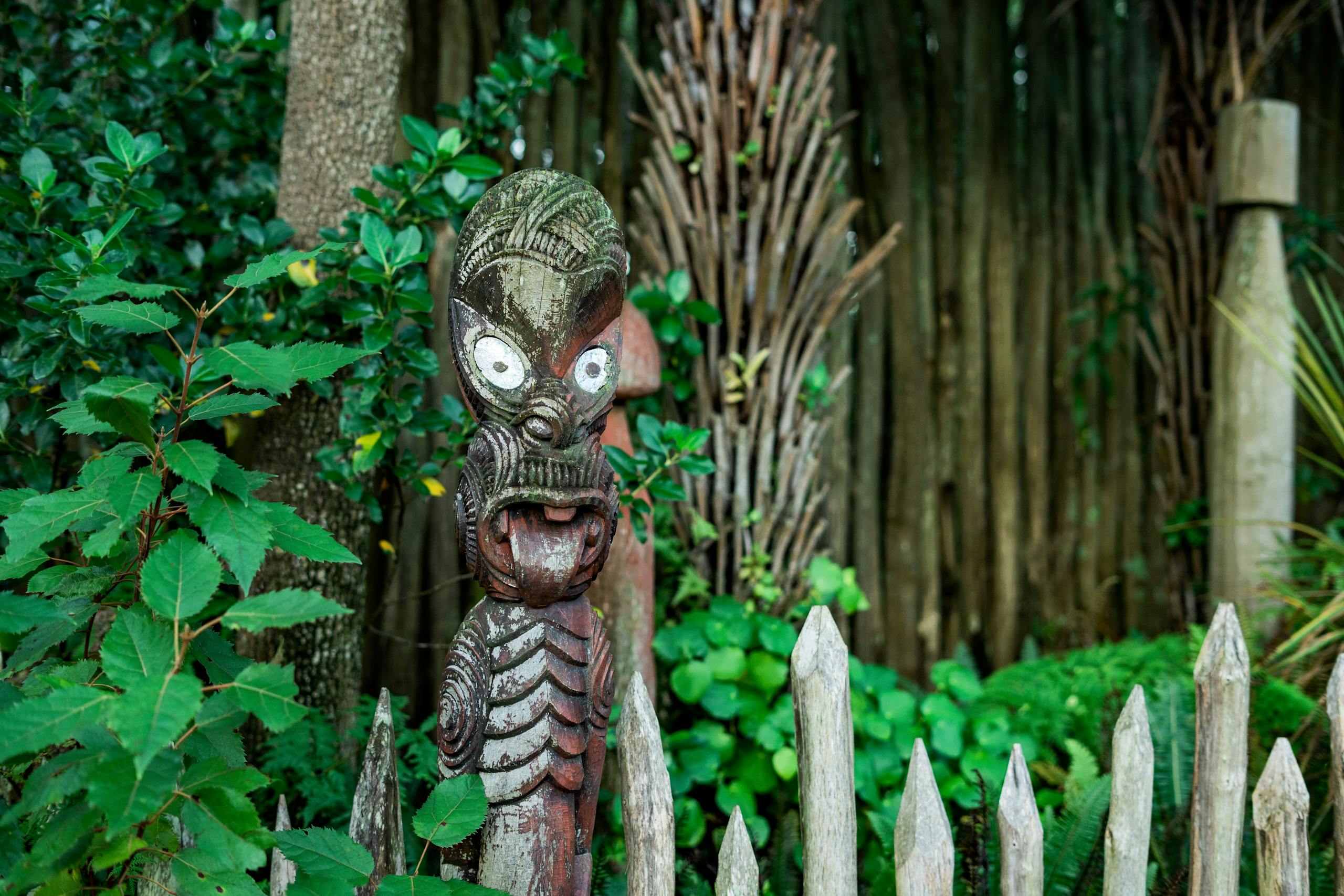 A traditional Maori carving surrounded by lush greenery in a New Zealand garden, showcasing cultural heritage.