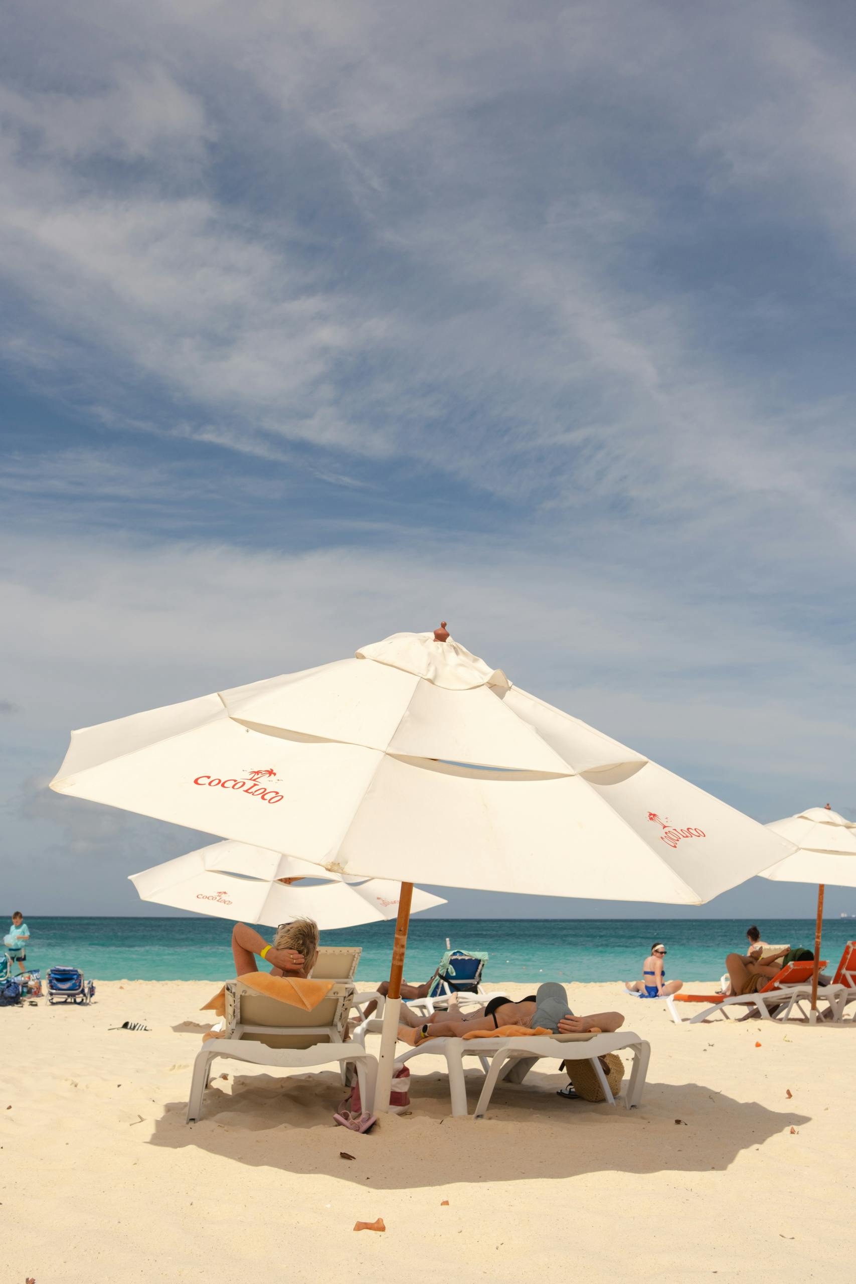 People enjoying a sunny day under white parasols on Eagle Beach. Perfect beach retreat in Aruba.