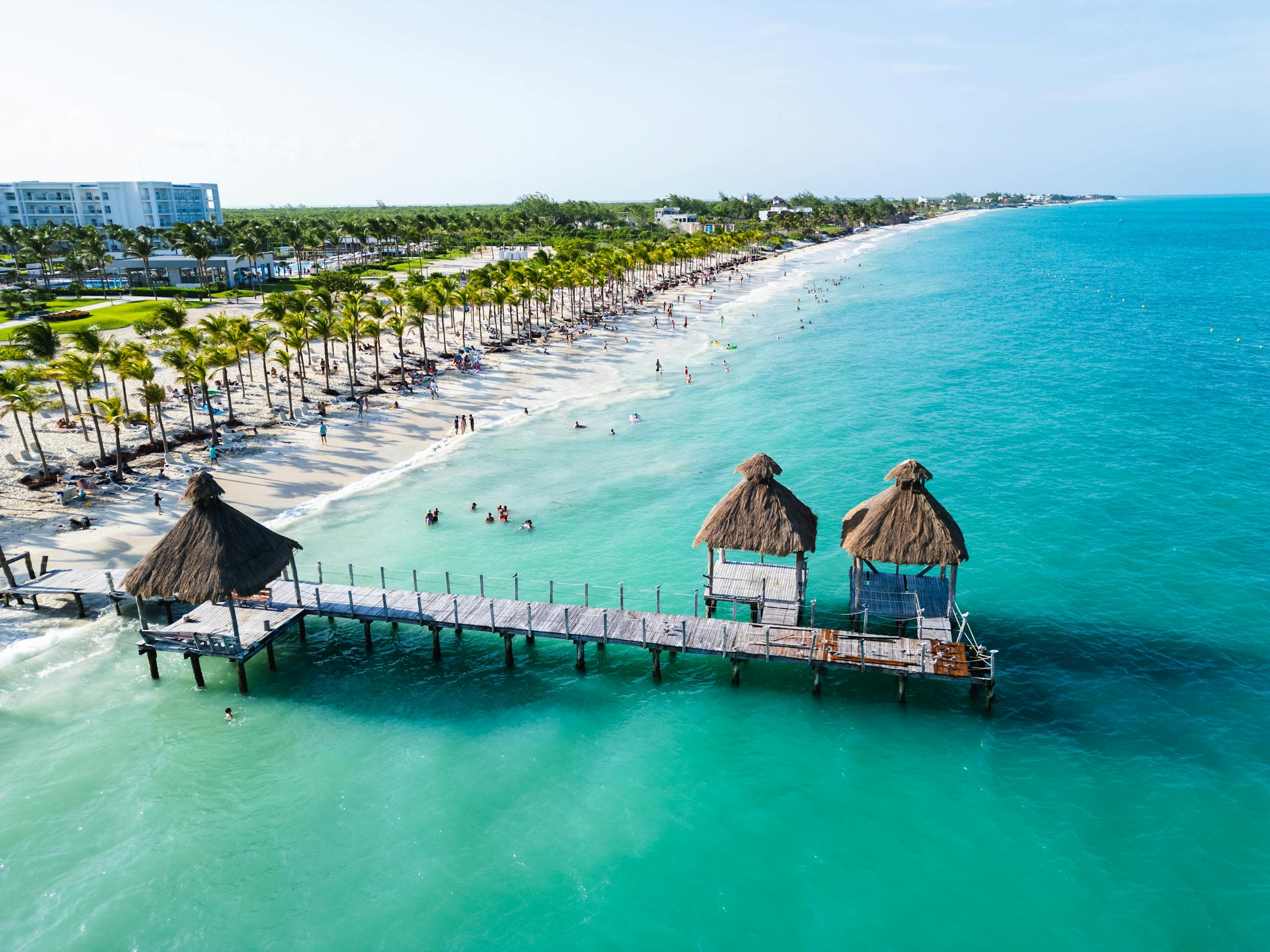 Stunning aerial view of Costa Mujeres beach with turquoise waters, palm trees, and a thatched pier.
