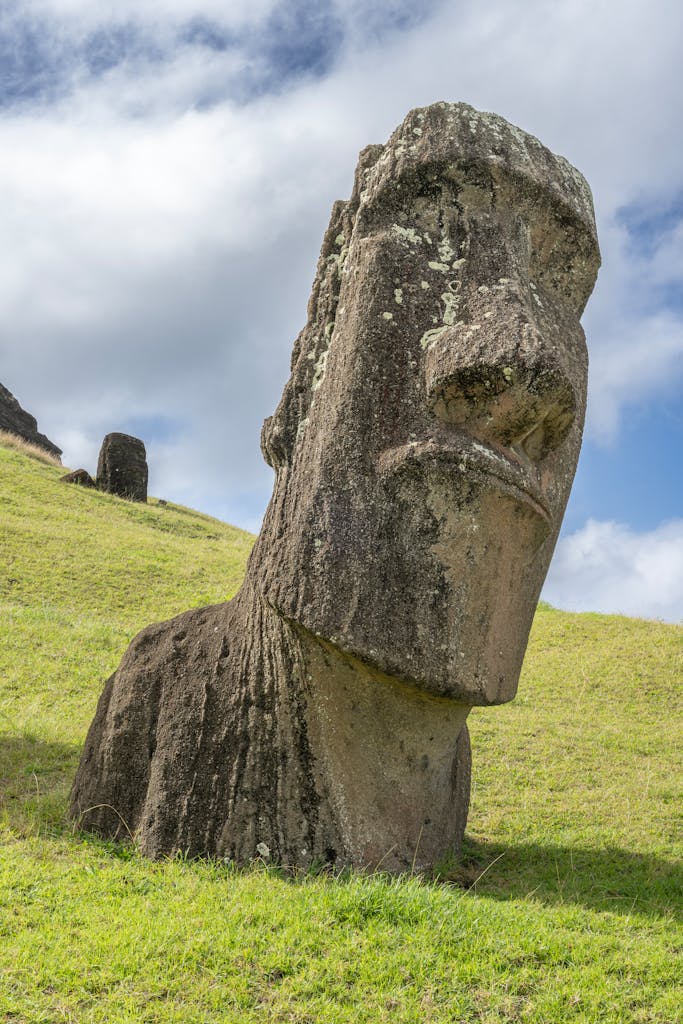 Stunning Moai statue on green hillside under a cloudy sky in Rapa Nui, Easter Island.